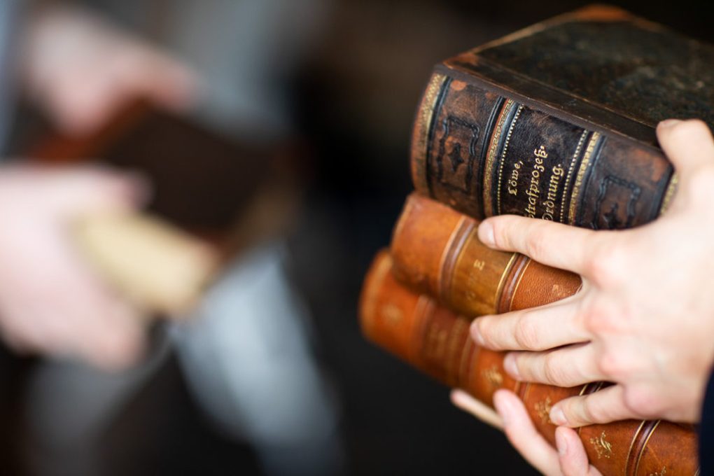 Eine Person hält einen Stapel von drei antiken Büchern juristischer Fachliteratur in den Händen.