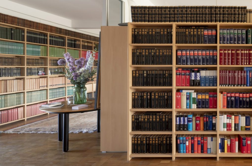 Eine Bibliothek mit vielfältiger juristischer Fachliteratur und einem eleganten Tisch mit einer Vase inklusive üppigem Blumenarrangement.