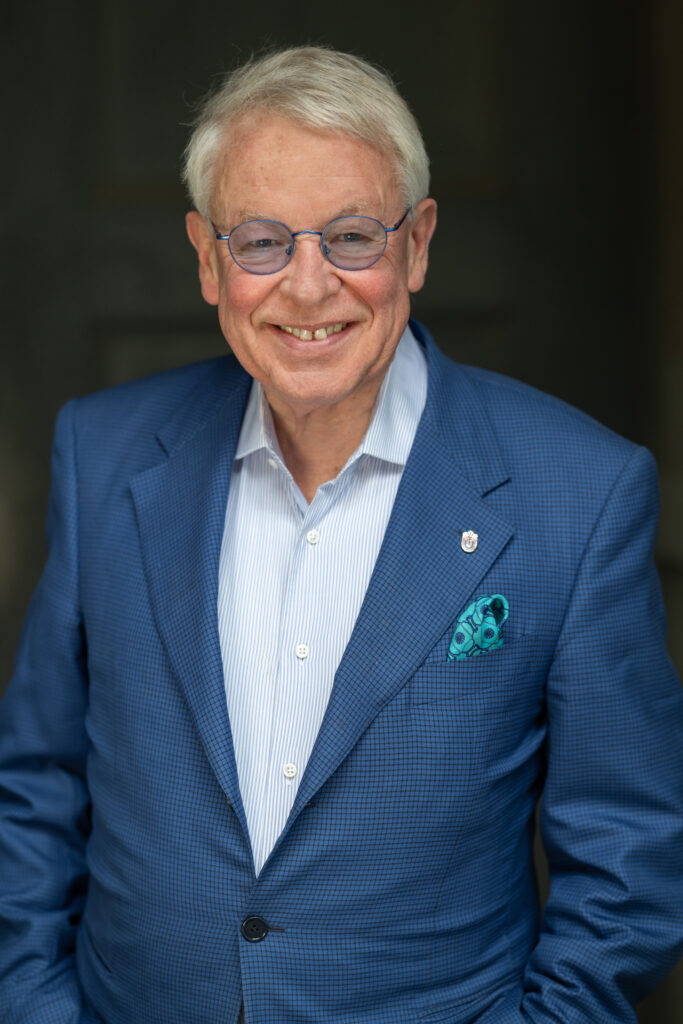 Dr. Gerhard Strate in einem blauen Jacket, lächelnd mit einer blauen Brille.